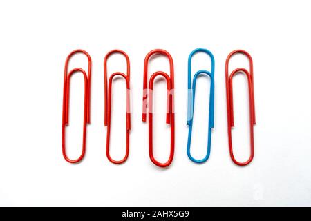 A blue paper clip amongst red paper clips stands out from the rest shot against a white background. Stock Photo