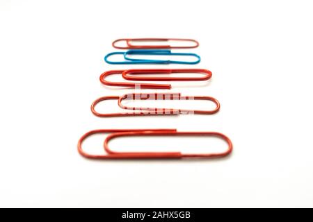 A blue paper clip amongst red paper clips stands out from the rest shot against a white background. Stock Photo