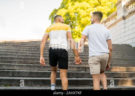 Portrait of happy gay couple spending time together and holding hands while walking in the street. Lgbt and love concept. Stock Photo