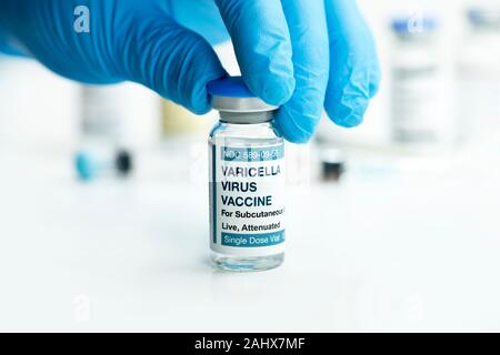 Varicella Virus vaccine vial chosen by gloved hand of heathcare professional with syringes and vaccines in background. Stock Photo