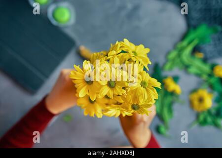 Woman puts a yellow chrysanthemum flowers in a glass transparent vase on the loft table