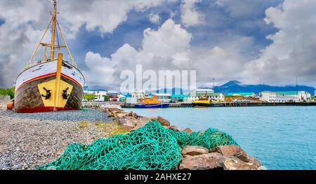 A commercial fishing harbor in a small coastal town in Iceland, with a green net in the foreground and an old wooden vessel out of the water. Stock Photo