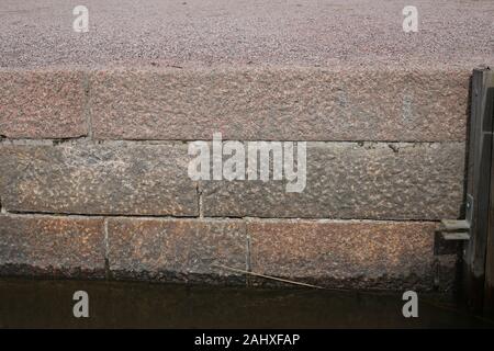 Weathered edge of an old pier made of big red tiles that are touching the sea water. Outdoor architecture details from Helsinki, Finland. Color image. Stock Photo