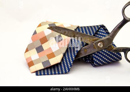 Two colourful ties being cut by a pair of old and large black scissors isolated on a white background in horizontal format Stock Photo