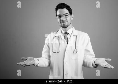 Portrait of young handsome man doctor against gray background Stock Photo