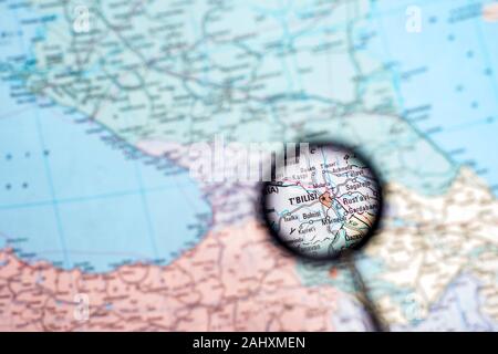 Georgia with the capital of Tbilisi close-up through a magnifying glass on the background of a blurred geographical map. Stock Photo