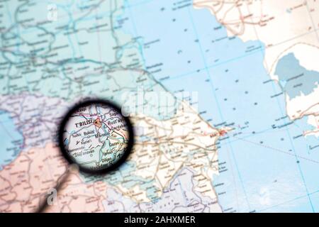 Georgia with the capital of Tbilisi close-up through a magnifying glass on the background of a blurred geographical map. Stock Photo