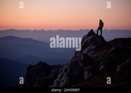 Woman standing on a rock at sunset, successful hiking silhouette in mountains, motivation and inspiration, Nanos Slovenija Stock Photo