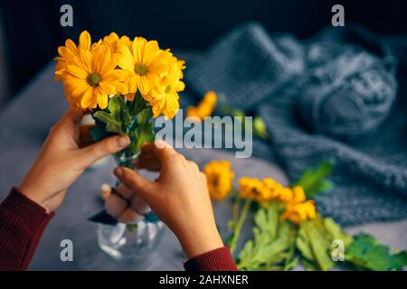 Woman puts a yellow chrysanthemum flowers in a glass transparent vase on the loft table