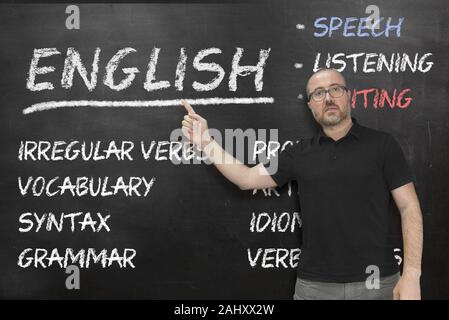 English teacher pointing to some language concepts writen on a blackboard in the classroom. Education concept with empty copy space for Editor's text. Stock Photo