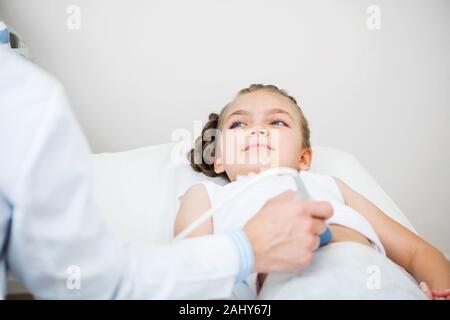 Sonographer moving transducer on belly of little girl. Modern clinical diagnostics and treatment. Close-up ultrasound scanner in male hand. Doctor exa Stock Photo