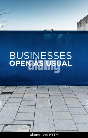 A business as usual sign on a hoarding around a demolition site in Basildon Town centre in Essex. Stock Photo