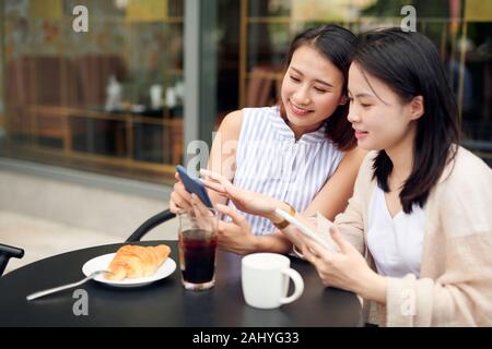 Two young women having coffee break together use smart phone. Happy women using cell phone at sidewalk cafe Stock Photo