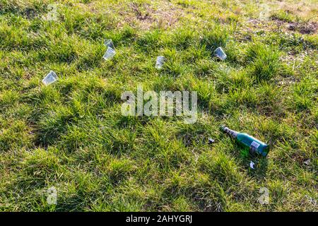 Empty bottle of champagne and plastic disposable single use glasses on grass after new years eve party Stock Photo