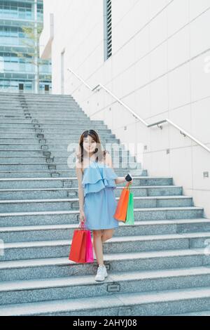 Modern Asian girl going down stairs and holding shopping bags. Shopaholic concept. Stock Photo