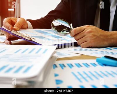 The auditor makes audit and verifies the report using a magnifying glass. Stock Photo