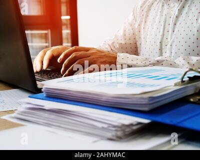 A man works at a computer in the office. Pile of financial performance papers. Stock Photo