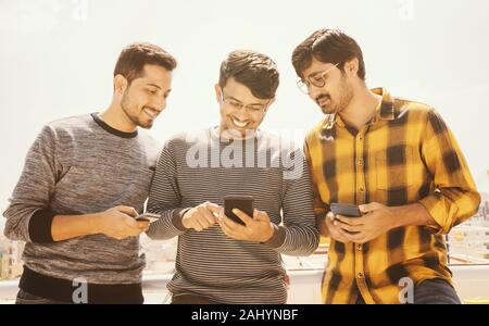 Group of young people watching mobile phone on terrace and laughing - friends using mobile phone againt the sunlight - Millennials on technology Stock Photo