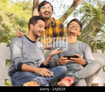 Group of friends laughing loud by watching into smartphone - Concept of young millennial people using technology, Social Media, Internet and mobile Stock Photo