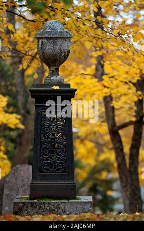 An old memorial on an ancient graveyard with beautiful yellow maple trees in autumn Stock Photo