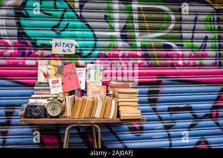 Books, a camera and an alarm clock are offered for sale in front of a gate with colorful graffity sprayed on in the suburb Karaköy Stock Photo