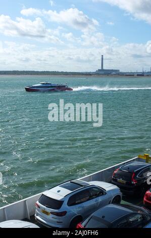 Fast Catamaran passenger ferry operated by Red Funnel passes Fawley Power Station on its route from Southampton to West Cowes on the Isle of Wight UK. Stock Photo