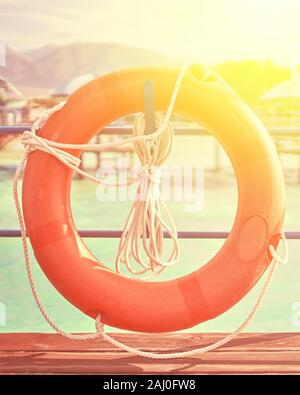 Orange lifebuoy with rope on a wooden pier near sea. Yellow ladder and an orange lifebuoy with rope on the pier in the background of the river. Stock Photo