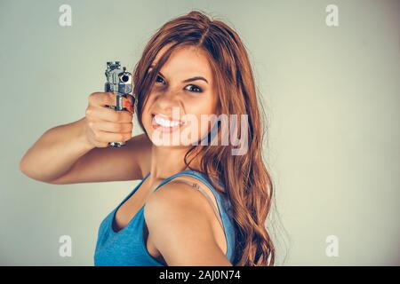 Beautiful young woman with a gun. Brunette holding Handgun looking, aimed, pointing at camera.Violent rebel gangster bandit self-justice concept. Mixe Stock Photo