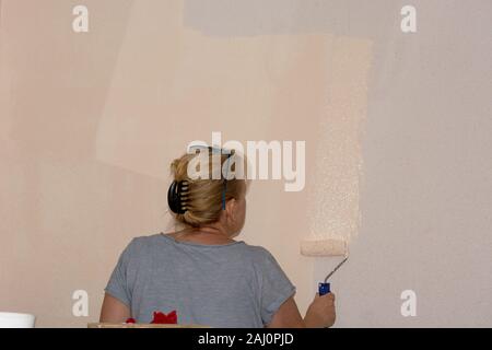 put up wall paper at home. Young woman, worker puts wallpapers on the wall. renovation concept Stock Photo
