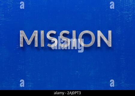 the word mission laid with silver metal characters on blue painted wooden board in central flat lay composition. Stock Photo