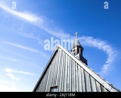 Church Steeple And Copy Space. Church steeple with wooden cross set against a blue sky with clouds and chem trails.