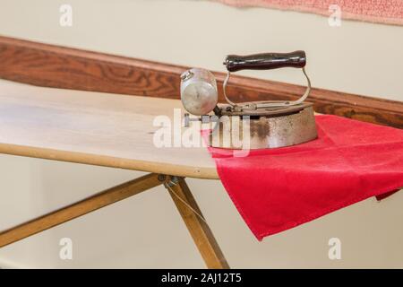Iron And Ironing Board. Old Fashioned metal clothes iron on wooden ironing board in horizontal orientation with copy space. Stock Photo