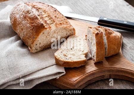 Loaf of whole wheat bread with slices on wooden board on kitchen table Stock Photo