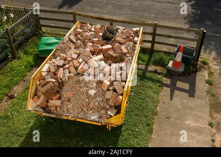 A skip full of building site rubble and bricks in the front garden of a residential property in Cheshire UK Stock Photo