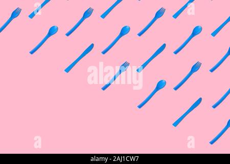 Flat lay of blue plastic disposable forks,spoons and knives pattern on pastel pink background minimal creative concept. Space for copy. Stock Photo