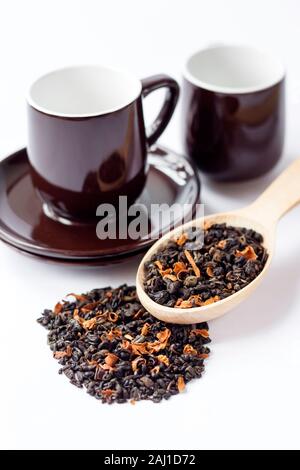 Dried green tea leaves with flower petals in wooden spoon and cup with saucer Stock Photo