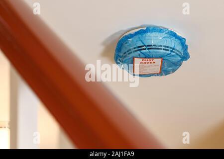 A blue polythene dust cover on a mains wired smoke alarm fitted in a UK domestic property Stock Photo