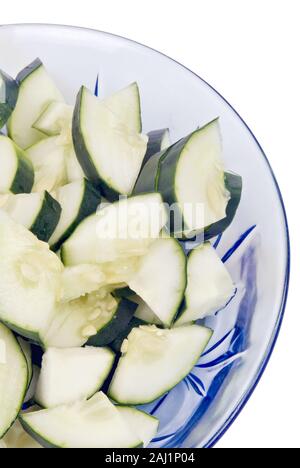 Sliced fresh cucumbers in a blue colored transparent glass bowl on an isolated white background. Stock Photo