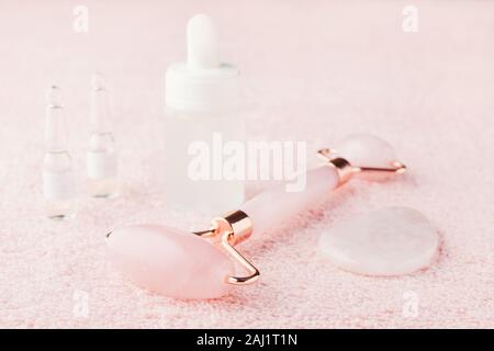 rose quartz facial roller, gua sha massage stone and face serum on pink Stock Photo