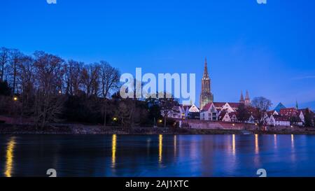 Germany, Ulm city skyline, cityscape and minster cathedral behind water of danube river in beautiful blue hour atmosphere by night after sunset Stock Photo