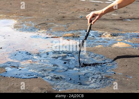 A woman's hand stirring liquid asphalt with a wooden stick at Pitch Lake, the largest natural deposit of bitumen in the world. La Brea, Trinidad islan Stock Photo