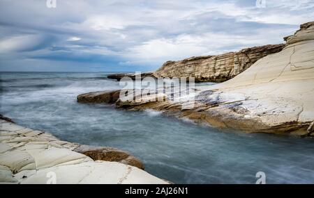 Rocky seashore seascape with wavy ocean and dramatic sky at the coastal area  in Limassol, Cyprus. Long exposure photography Stock Photo