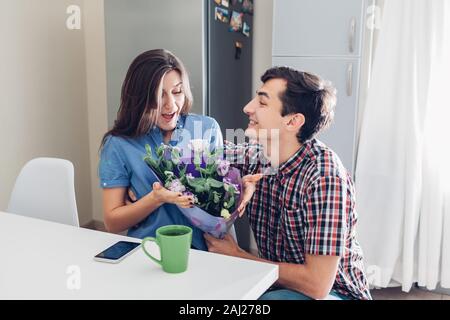 Man gifting bouquet of flowers to his girlfriend on kitchen at home. Valentines day romantic surprise. Happy couple in love Stock Photo