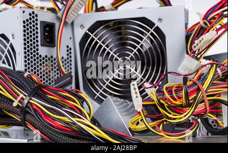 Computer power supply units detail on pile with colored cables and peripheral connectors. Tangle of insulated wires. Fan in square metal box. E-waste. Stock Photo