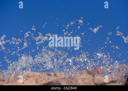 Water droplets spraying from a fountain in abstract design on blue sky and orange background and detail and contrast. Concept. Stock Photo