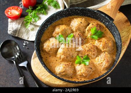 Meatballs in sour cream and tomato sauce in a pan on a dark stone or slate table. Stock Photo