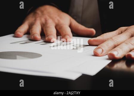 Closeup of businessman reviewing report paper with graphs and pie charts in a conceptual image. Stock Photo