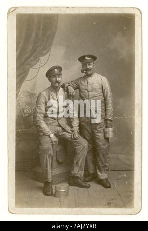 Original WW1 era portrait postcard of two cheerful men in the British Army Service Corps (ASC) at the Front in France. The friends are wearing fatigues and caps wearing the ASC badge, and carry a mess tin which may indicate they are soldier regimental cooks working in a field kitchen. Both men are smoking a pipe. U.K. date on reverse is 27 November 1917 and was sent from the Front in France. Stock Photo