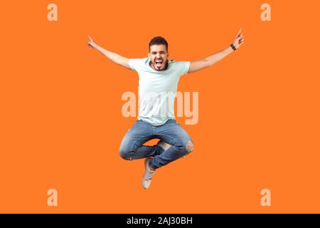 Full length of crazy overjoyed brunette man in white outfit jumping in air with raised hands, screaming loud for joy, feeling energetic and lively. in Stock Photo