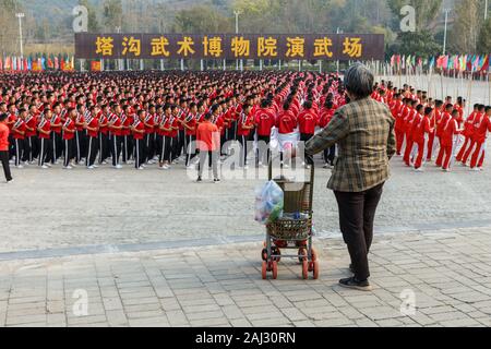 Dengfeng, China - October 17, 2018: An elderly woman with a child in a stroller looks at the pupils of the martial arts school at the Shaolin monaster Stock Photo